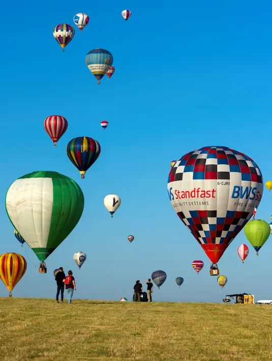 Pengunjung menyaksikan balon udara terbang di pangkalan udara Chambley-Bussieres, Hagéville, Prancis, Senin (29/7/2019). Festival balon udara tersebut dimanfaatkan para pilot balon udara untuk berkumpul. (Jean-Christophe VERHAEGEN/AFP)