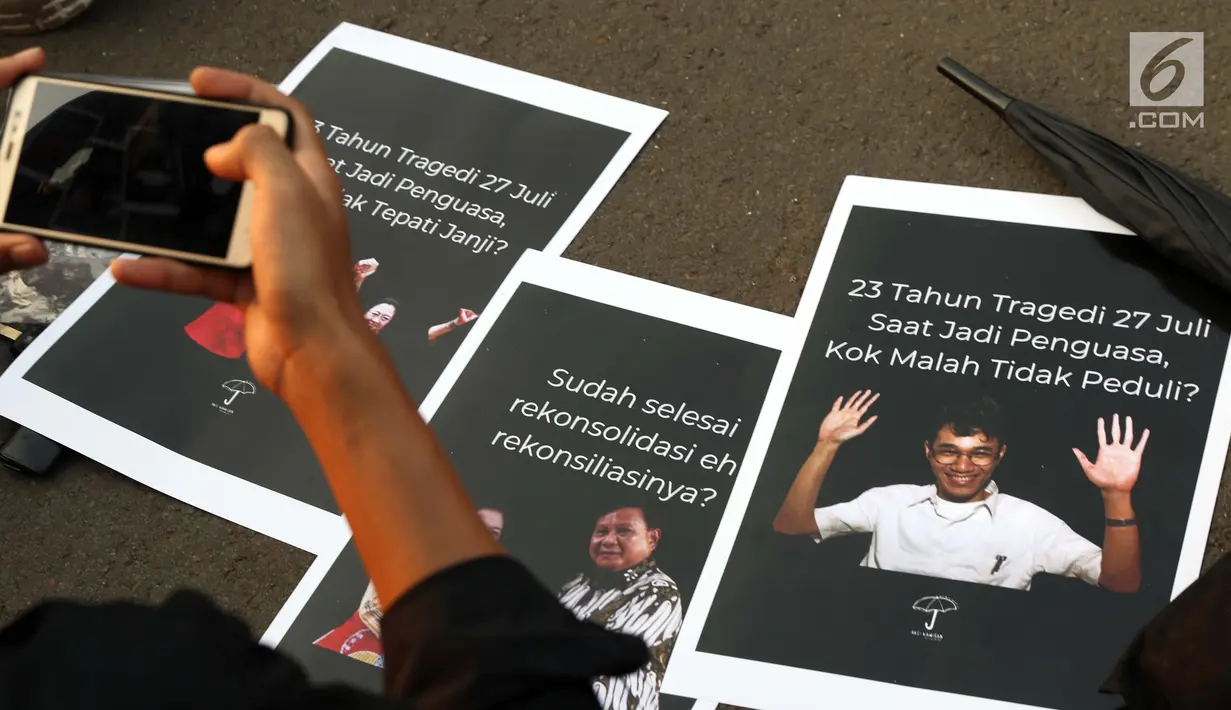Aktivis yang tergabung dalam Jaringan Solidaritas Korban untuk Keadilan memotret poster saat aksi Kamisan di depan Istana Negara, Jakarta, Kamis (25/7/2019). Aksi Kamisan ke-594 mengangkat tema '23 Tahun Tragedi 27 Juli Saat Jadi Penguasa Kok Malah Tidak Peduli?'. (Liputan6.com/Helmi Fithriansyah)