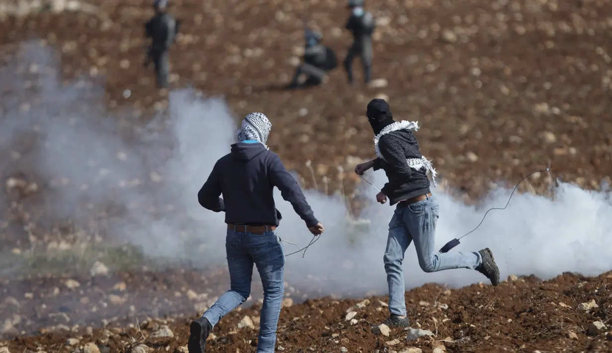 Pengunjuk rasa Palestina menggunakan ketapel untuk melemparkan batu ke arah pasukan Israel selama protes terhadap pemukiman Israel, di desa Deir Jarir Tepi Barat, utara Ramallah, Jumat (1/1/2021). (AP Photo/Majdi Mohammed)