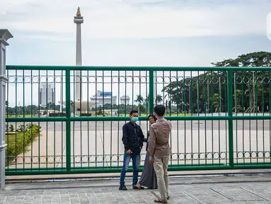 Warga berfoto di belakang Monumen Nasional atau Monas di Jakarta, Jumat (1/1/2021). Walaupun Monas ditutup warga tetap memanfaatkan libur Tahun Baru untuk berwisata dan berfoto di kawasan Monas. (Liputan6.com/Faizal Fanani)