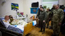 Dalam foto yang disediakan oleh Kantor Pers Kepresidenan Ukraina pada 13 Maret 2022, Presiden Ukraina Volodymyr Zelenskyy (tengah) berbicara dengan seorang tentara yang terluka saat kunjungannya ke sebuah rumah sakit di Kiev, Ukraina. (Ukrainian Presidential Press Office via AP)
