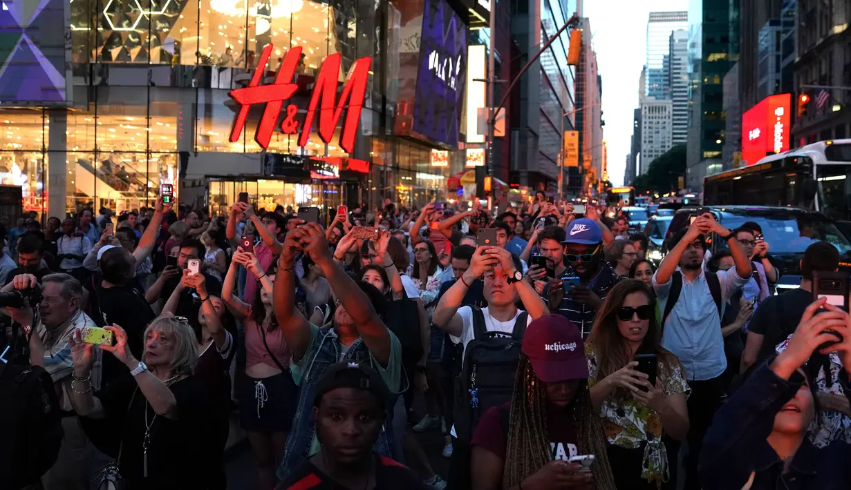 Orang-orang mengambil gambar fenomena Manhattanhenge, dimana matahari terbenam sejajar tepat dengan jalan, di 42nd street di Times Square, New York City, Kamis (12/7). Fenomena ini hanya terjadi selama beberapa hari dalam setahun. (AFP/TIMOTHY A. CLARY)