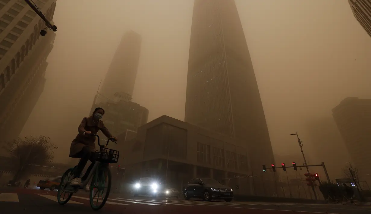 Pesepeda melewati gedung-gedung perkantoran di tengah badai pasir pada jam sibuk pagi hari di kawasan pusat bisnis di Beijing, Senin (15/3/2021). (AP Photo/Andy Wong)