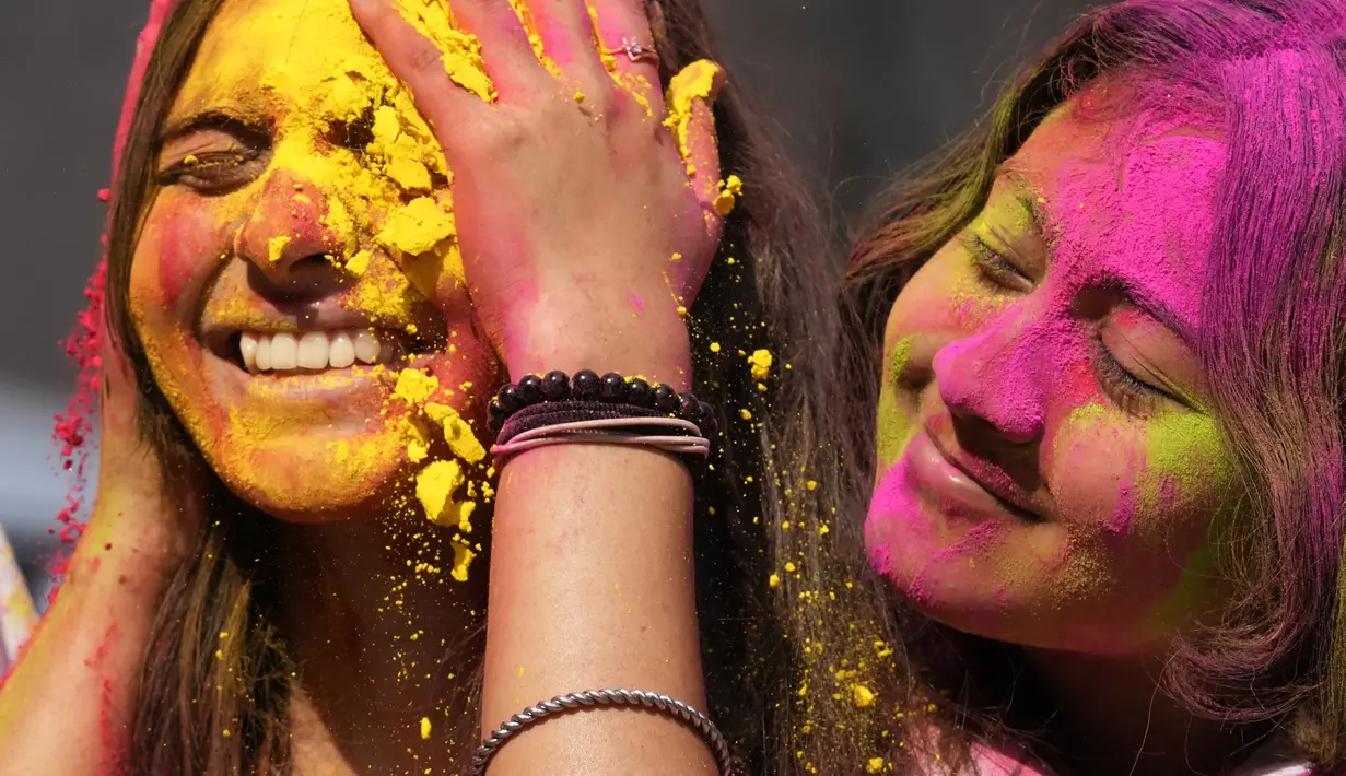 Orang yang bersuka ria mengolesi bedak berwarna di wajah orang lain selama perayaan menandai Holi, festival warna Hindu, di Mumbai, India (18/3/2022).  Holi, festival warna Hindu, juga menandai datangnya musim semi. (AP Photo/Rajanish Kakade)