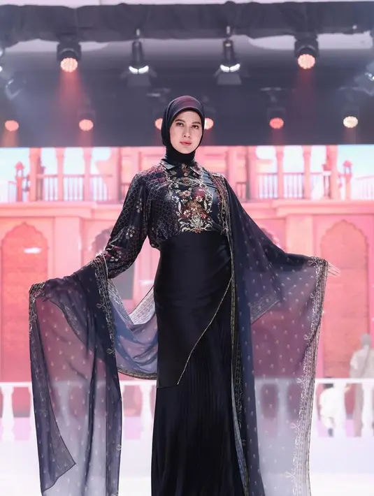 Paula Verhoeven tampil memikat dalam balutan dress hitam yang jatuh sleek mengikuti siluet tubuh. Detail motif bold dan selendang sheer memberi kesan teatrikal sekaligus mempertegas karakter koleksi yang bold. [Dok/Shi by Shireen & Zaskia Sungkar].