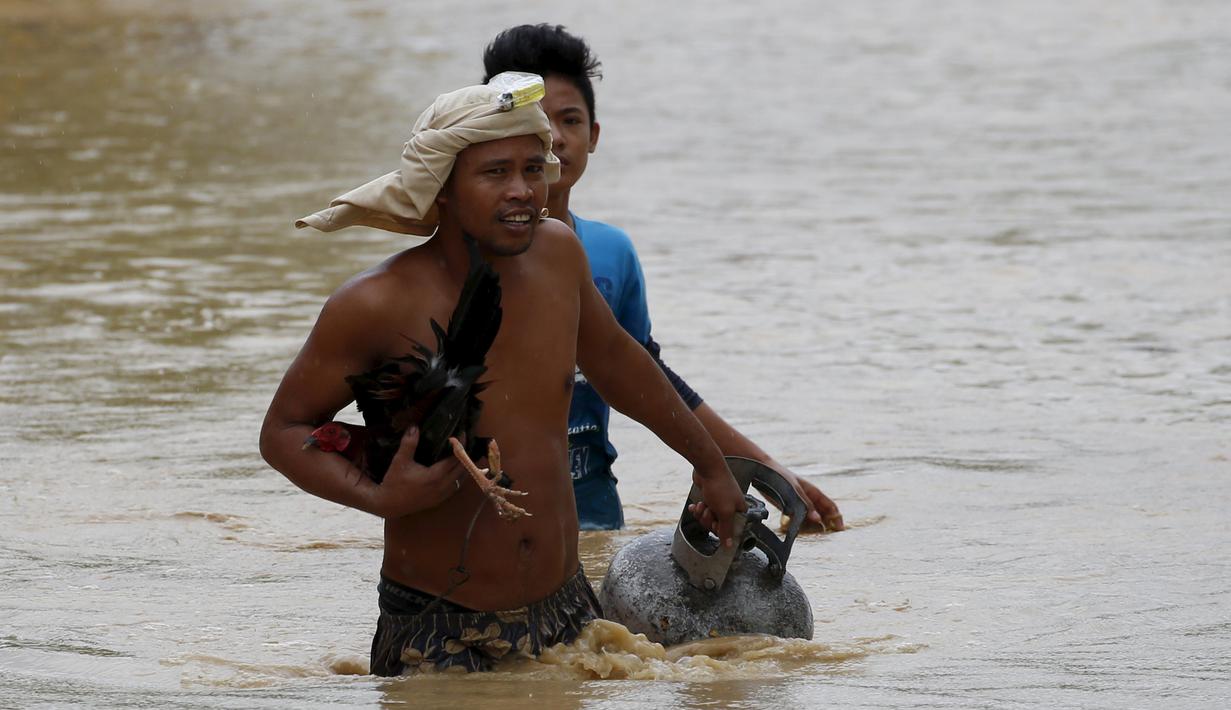 Seorang warga tampak membawa tabung gas dan hewan peliharaanya melewati jalanan yang banjir pasca bencana badai topan Koppu di Nueva Ecija,  Filipina, Senin (19/10/2015). Badai terjadi pada Minggu pagi waktu setempat. (REUTERS/Erik De Castro)