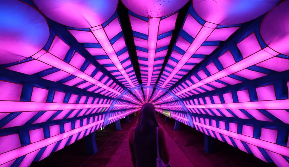 Seorang wanita berjalan melewati instalasi lampu di Dubai Garden Glow, Dubai, Uni Emirat Arab, 1 November 2021. Instalasi tersebut dibuat dari lebih satu juta bohlam penghemat energi dan kain bercahaya daur ulang karya seniman seluruh dunia. (GIUSEPPE CACACE/AFP)