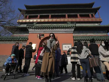 Seorang perempuan berswafoto dengan haw China berlapis gula saat pengunjung berkumpul di luar Menara Drum di Beijing, Senin (30/1/2023). Orang-orang China menikmati Tahun Baru Imlek dan mengunjungi berbagai lokasi wisata di kota-kota di sekitar China setelah pencabutan pembatasan COVID-19 yang kejam bulan lalu, memungkinkan banyak aspek kehidupan normal kembali. (AP Photo/Andy Wong)