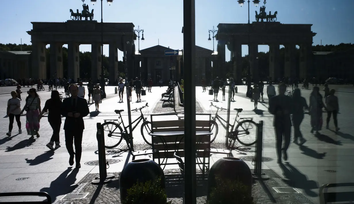 Orang-orang terpantul di jendela saat mereka berjalan di depan Gerbang Brandenburg, saat cuaca hangat, di Berlin, Jerman, Kamis  (6/8/2020). (AP Photo / Markus Schreiber)