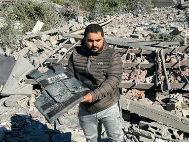 Seorang pria memegang rompi rusak bertuliskan “Press” di tengah puing-puing lokasi serangan udara Israel yang menargetkan area di mana sejumlah wartawan berada di desa Hasbaya, Lebanon selatan, pada Jumat 25 Oktober 2024. (Ali Hankir/AFP)