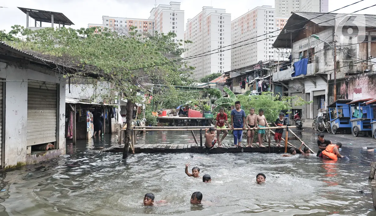 Anak-anak berenang di kali yang masih meluap ke permukiman Kampung Rawa Indah, Jakarta Utara, Senin (24/2/2020). Kampung yang terletak di dua kelurahan, yakni Sukapura dan Pegangsaan Dua tersebut masih terendam banjir hingga sore ini dengan ketinggian air 30-50 cm. (merdeka.com/Iqbal S Nugroho)