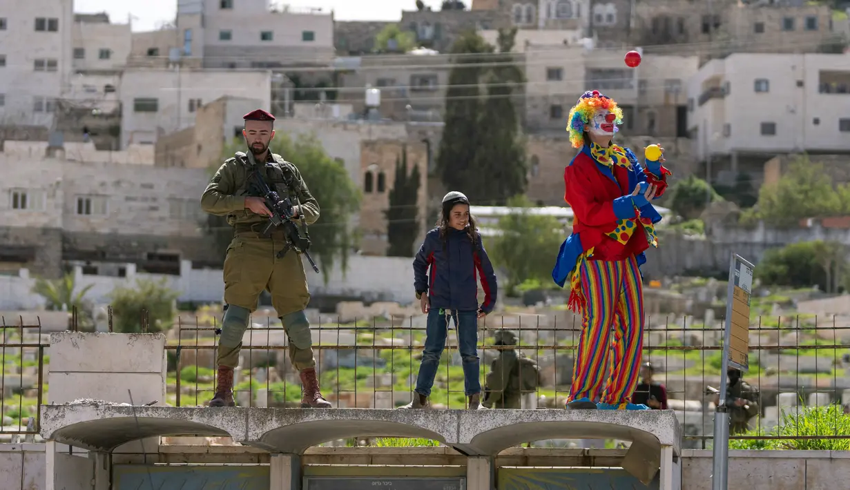 Pemukim Yahudi yang mengenakan kostum merayakan Hari Raya Purim saat tentara mengamankan pawai di Kota Hebron, Tepi Barat, 7 Maret 2023. Para pemukim setiap tahun mengadakan parade perayaan Hari Raya Purim untuk memperingati keselamatan orang Yahudi dari genosida di Persia kuno, seperti yang diceritakan dalam Gulungan Ester. (AP Photo/Ohad Zwigenberg)