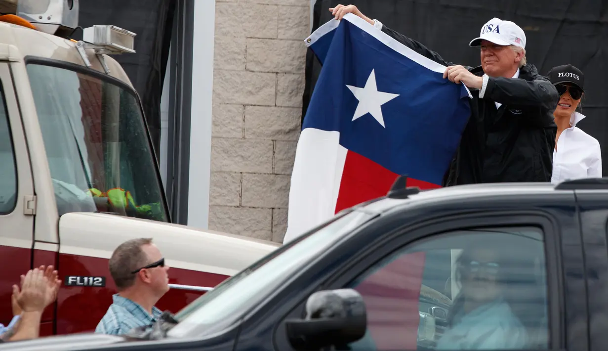 Presiden AS, Donald Trump mengibarkan bendera Texas di hadapan warga yang bersorak padanya di Firehouse 5 in Corpus Christi, Selasa (29/8). Trump mencoba menyemangati warganya lewat kunjungan ke Texas yang dihantam badai Harvey. (AP Photo/Evan Vucci)