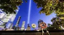 Karangan bunga peringatan ditinggalkan di 9/11 Memorial & Museum saat Tribute in Light tahunan memproyeksikan dua pilar cahaya ke langit malam di New York City (10/9/2021). Cahaya kembar itu untuk peringati serangan 11 September 20 tahun silam. (AFP/Roberto Schmidt)