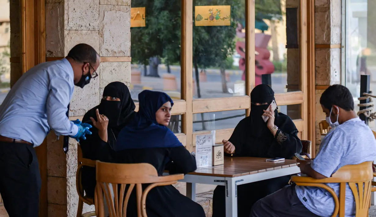 <p>Pelayan mengenakan sarung dan masker melayani pelanggan di sebuah kafe di ibu kota Arab Saudi, Riyadh (21/6/2020). (AFP Photo/Fayez Nureldine)</p>