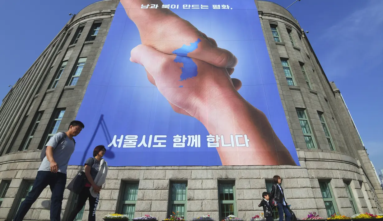 Pejalan kaki berjalan melewati spanduk yang menunjukkan foto dua tangan bersalaman dengan gambar peta Semenanjung Korea di Seoul, Korea Selatan (18/4). Spanduk ini bertujuan untuk mendukung pertemuan antara Korut dan Koresel. (AFP Photo/Jung Yeon-je)