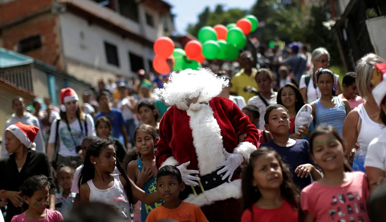 Santa Claus berjalan bersama kerumunan anak-anak di kawasan kumuh Petare di Caracas, Venezuela (11/12). Petare adalah sebuah kawasan yang masuk dalam ibukota Caracas dan terkenal kumuh. (Reuters/Ueslei Marcelino)