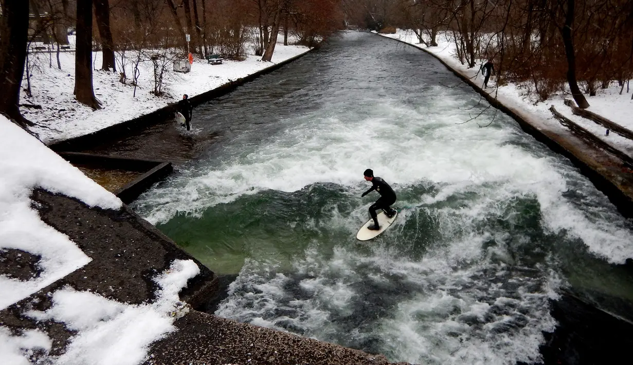 Aksi peselancar menaklukkan ombak saat berselancar di Sungai Eisbach selama hari musim dingin di Munich, Jerman, 4 Januari 2017. Aliran air Eisbach yang memiliki  lebar 12 meter ini berasal dari sungai Isar.  (Mark RALSTON/AFP)