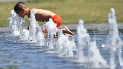 Seorang anak mendekatkan wajahnya pada air mancur saat menikmati musim panas di Nantes, Prancis barat, Senin (19/6). Suhu temperatur di Prancis mencapai 36 derajat celcius. (AFP Photo / LOIC VENANCE)
