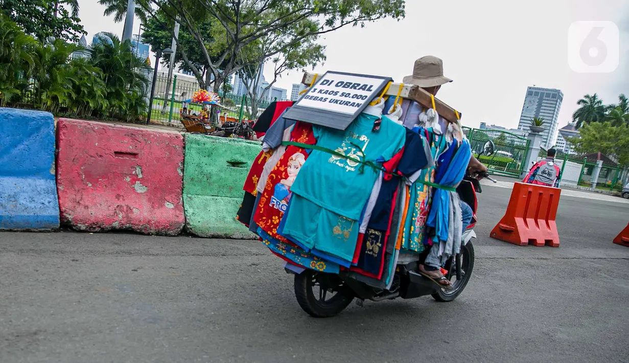 Pedagang kaos cendera mata berkeliling untuk berjualan di kawasan Monas, Jakarta, Sabtu (2/1/2021). Pemerintah Provinsi DKI Jakarta menutup sejumlah tempat wisata selama masa libur Tahun Baru dari 25 dan 31 Desember 2020, serta 1 Januari 2021. (Liputan6.com/Faizal Fanani)