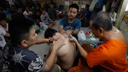 Sejumlah orang menyaksikan seorang pria yang di tato menggunakan jarum tradisional di Wat Bang Phra, Nakhon Pathom, Thailand , (18/3). Orang-orang rela antri untuk mendapat tato dari guru pembuat tato atau Biksu tersebut. (REUTERS / Chaiwat Subprasom)