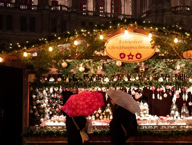 Wisawatan menggunakan payung saat mengunjungi pasar Natal di luar City Hall, Wina pada 26 November 2018. Di Pasar Natal ini, para pengunjung bisa menikmati jajanan khas hingga pernak-pernik kerajinan tangan asli Austria. (JOE KLAMAR / AFP)