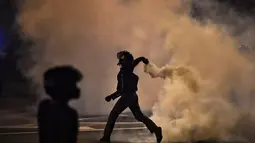 Seorang pengunjuk rasa melemparkan tabung gas air mata selama bentrokan dengan polisi di Bangkok, Thailand, Minggu (6/9/2021). Mereka memprotes ketidaksetujuan terhadap cara pemerintah Thailand menangani pandemi dan pemberian vaksin Covid-19. (AFP/Jack Taylor)