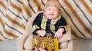 Baby Moana tampil tersenyum saat mengenakan busana adat Jawa Tengah. Ia mengenakan kebaya mungil berwarna hitam emas berpadu dengan kain batik cokelat. Tak ketinggalan aksesori kepala yang cantik berwarna emas. (instagram/rittarrajagukguk)