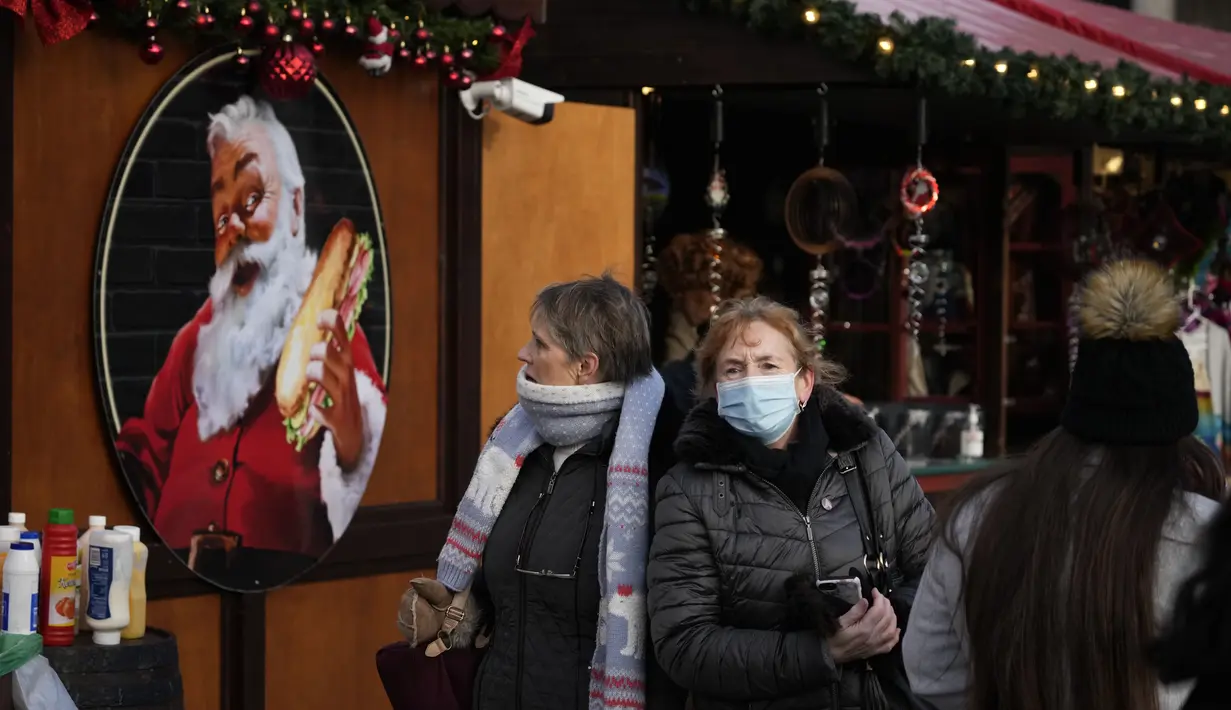 Orang-orang melewati gambar Sinterklas di sisi sebuah kios di pasar Natal, di Trafalgar Square, London, Senin (29/11/2021). Di Inggris, kewajiban mengenakan masker akan berlaku lagi di toko-toko dan transportasi umum mulai Selasa menyusul temuan Covid-19 varian Omicron. (AP Photo/Matt Dunham)