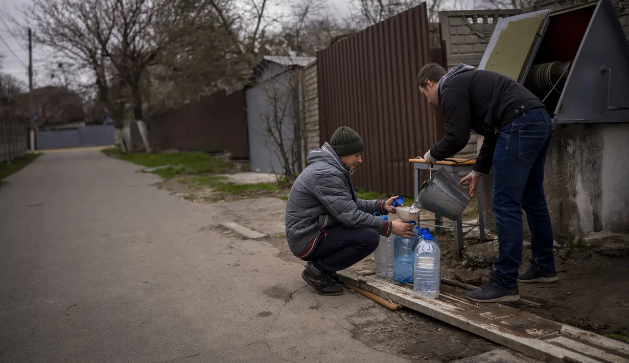 Dua pria Ukraina mengisi botol dengan air yang mereka ambil dari air mancur umum di Bucha, di pinggiran Kiev, Ukraina pada Senin (18/4/2022). Warga Bucha masih tanpa listrik, air dan gas setelah lebih dari 43 hari sejak invasi Rusia. (AP Photo/Emilio Morenatti)