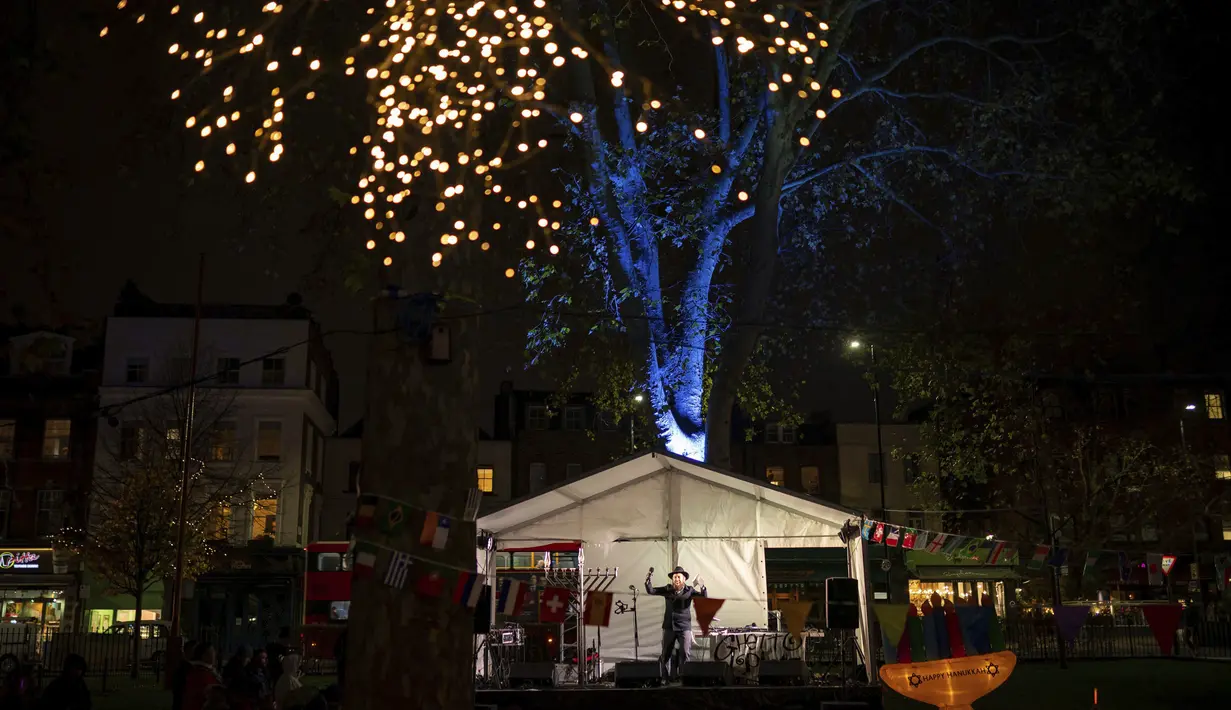 Rabi Mendy Korer di atas panggung saat Menorah dinyalakan di Islington Green di London utara, Minggu (28/11/2021). Perayaan tahunan komunitas malam pertama Hanukkah kembali dengan kapasitas penuh tahun ini setelah perayaan dibatasi pada tahun 2020 karena pandemi virus corona. (AP Photo/Aaron Chown)