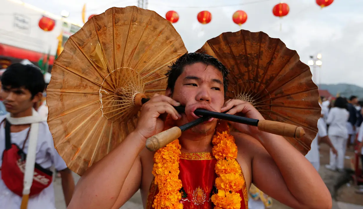 Seorang pemuja dari Kuil Samkong menusukkan dua payung pada pipinya ketika beratraksi dalam Festival Vegetarian di Phuket, Thailand, Selasa (4/10). (REUTERS/Jorge Silva)
