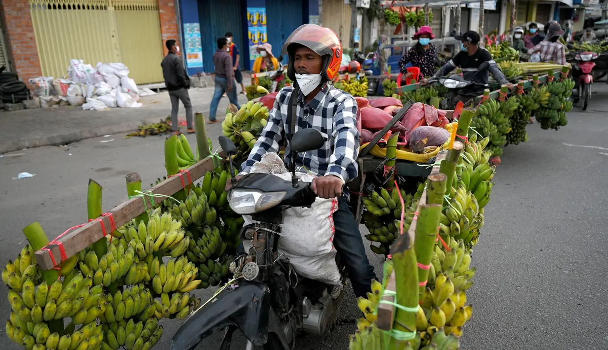 Seorang pedagang mengendarai sepeda motor bermuatan pisang di sepanjang jalan di Phnom Penh (13/10/2021). Pisang ditawarkan untuk dijual oleh pedagang keliling di jalan-jalan Phnom Penh, Kamboja. (AFP/Tang Chhin Sothy)