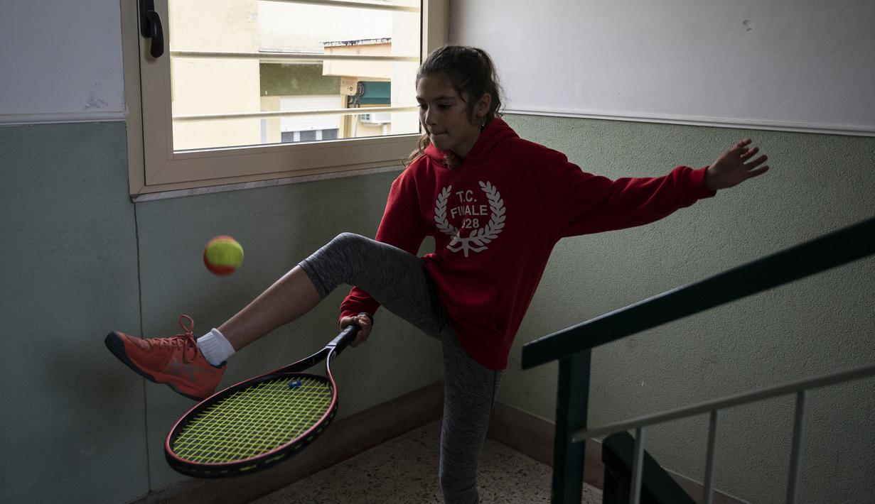 Carola Pessina berlatih sebelum bermain tenis dengan Vittoria Oliveri di atap rumah mereka selama lockdown COVID-19 di Finale Ligure, Italia (19/4/2020). Setiap hari Carola, 11, dan Vittoria, 13, bermain tenis dari satu atap ke atap lain di rumah mereka untuk berlatih. (AFP/Marco Bertorello)