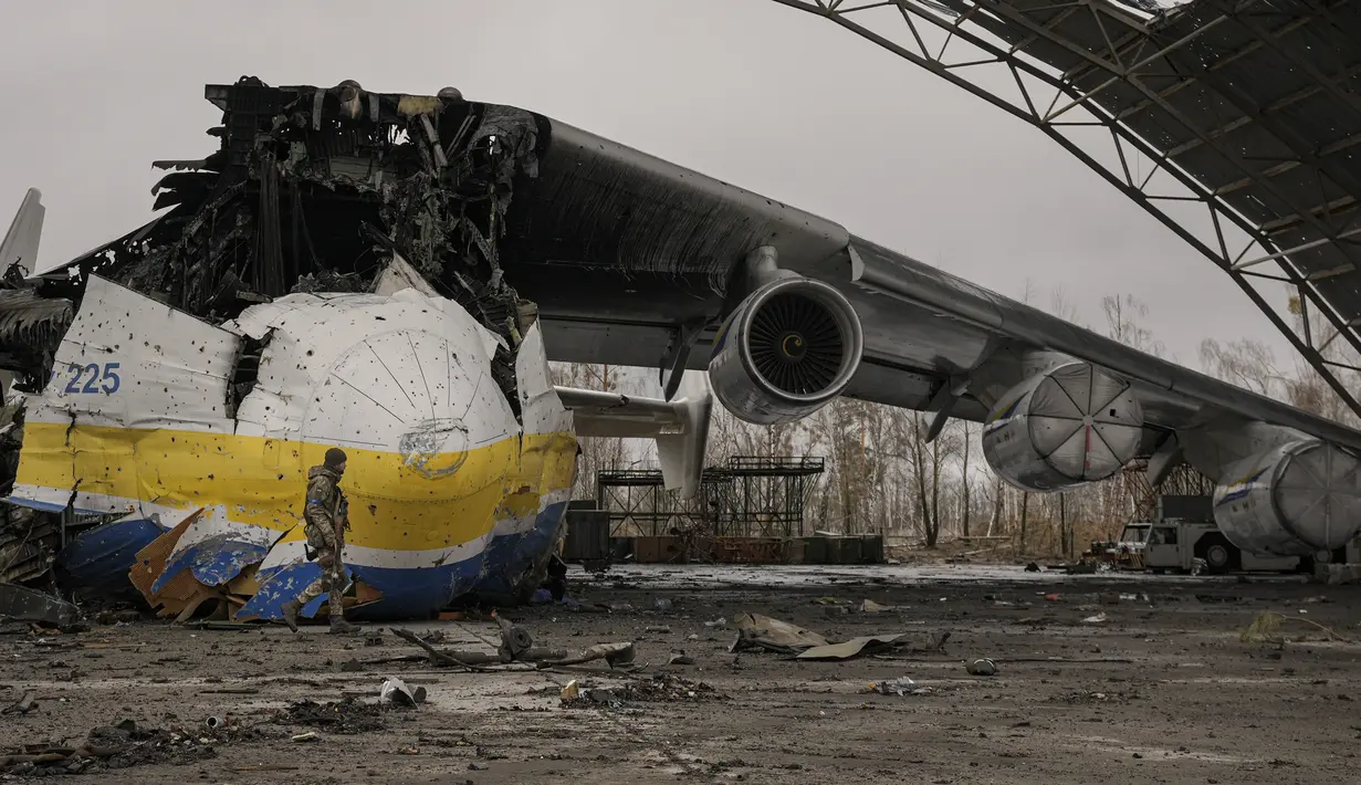 Prajurit Ukraina melewati pesawat Antonov An-225 Mriya yang hancur di bandara Antonov, Hostomel, 2 April 2022. Di pintu masuk Bandara Antonov, pasukan menjaga posisinya, tanda mereka memegang kendali penuh atas landasan pacu yang coba diserbu Rusia di hari-hari pertama perang (AP Photo/Vadim Ghirda)