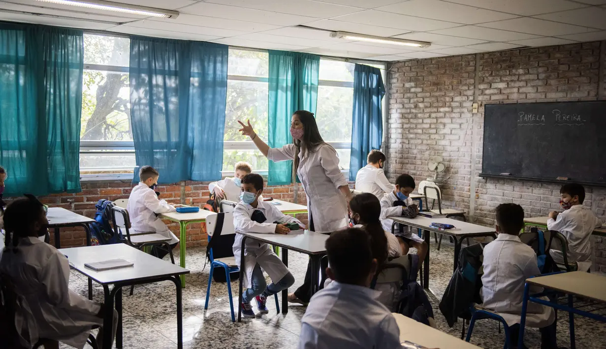 Seorang guru berbicara kepada siswa pada hari pertama mereka kembali ke kelas tatap muka di tengah pandemi COVID-19 di sekolah umum di Montevideo, Uruguay (1/3/2021).  Uruguay mengembalikan sebagian besar siswanya ke kelas tatap muka setelah liburan musim panas. (AP Photo/Matilde Campodonico)