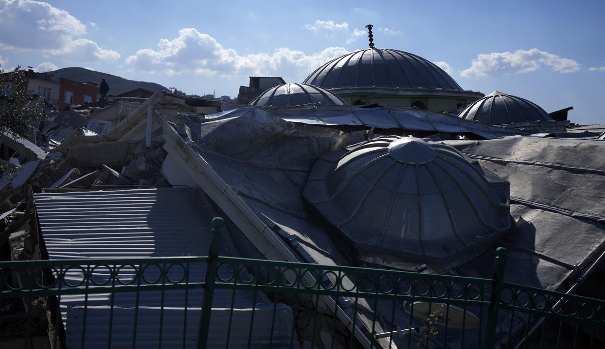Seorang pria (kiri atas) berdiri di atas sisa-sisa masjid yang hancur akibat gempa Turki di Antakya, Turki selatan, Rabu, 8 Februari 2023. Tim pencari dari lebih dari dua lusin negara telah bergabung dengan puluhan ribu personel darurat lokal di Suriah dan Turki. (AP Photo/Khalil Hamra)
