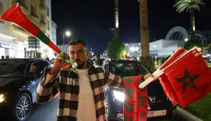 Seorang pria Maroko meniup vuvuzela sambil menjual bendera nasional di Rabat selama perayaan setelah kemenangan tim mereka di final Piala Arab 2025 antara Yordania dan Maroko yang berlangsung di Stadion Lusail, Lusail pada 18 Desember 2025. (Abdel Majid BZIOUAT/AFP)