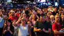 Orang-orang menonton atraksi aerialist Nik Wallenda dan saudara perempuannya Lijana Wallenda melintasi seutas kawat di ketinggian 396 meter, Times Square, New York, AS, Minggu (23/6/2019). Nik dan Lijana berasal dari keluarga pemain sirkus Flying Wallendas (vah-LEN’-dash). (Johannes EISELE/AFP)