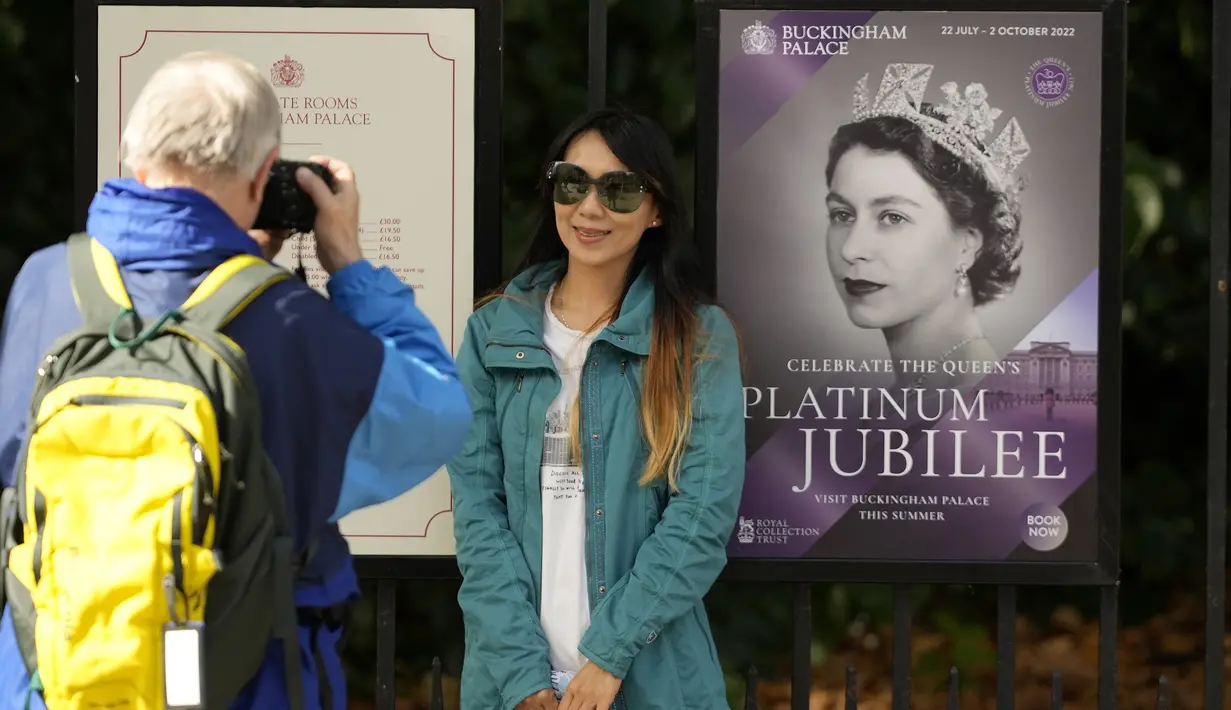 Turis berfoto di samping poster Ratu Elizabeth II di pagar Istana Buckingham di London, Kamis (8/9/2022). Pengumuman itu muncul sehari setelah ratu membatalkan pertemuan virtual Dewan Penasihatnya ketika dokter menyarankannya untuk beristirahat setelah sehari penuh acara pada hari Selasa, ketika dia secara resmi meminta Liz Truss untuk menjadi perdana menteri. (AP Photo/Frank Augstein)