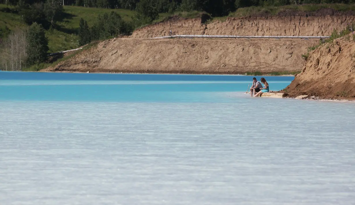 Sepasang suami istri bersantai dekat tempat pembuangan abu dari pabrik batubara lokal di Danau Novosibirsk, Rusia, Kamis (11/7/2019). Saking populernya, danau yang sepintas mirip oasis itu  bahkan memiliki akun instagramnya sendiri, yakni @maldives_nsk. (Rostislav NETISOV/AFP)