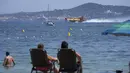 Wisatawan menyaksikan pesawat pelempar air mengisi tangkinya di pantai di Sainte-Maxime, Prancis selatan, Rabu (18/8/2021). Lebih dari 1.100 petugas pemadam kebakaran berjuang melawan api dan ribuan turis dan penduduk lokal dievakuasi ke daerah yang lebih aman. (AP Photo/Daniel Cole)