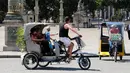 Wisatawan berkeliling kota Paris menggunakan transportasi becak, Prancis, (7/7). Desain becak di Paris ini memiliki posisi penarik becak dibagian depan berbeda dengan becak yang ada di Indonesia. (AFP Photo/Jacques Demarthon)