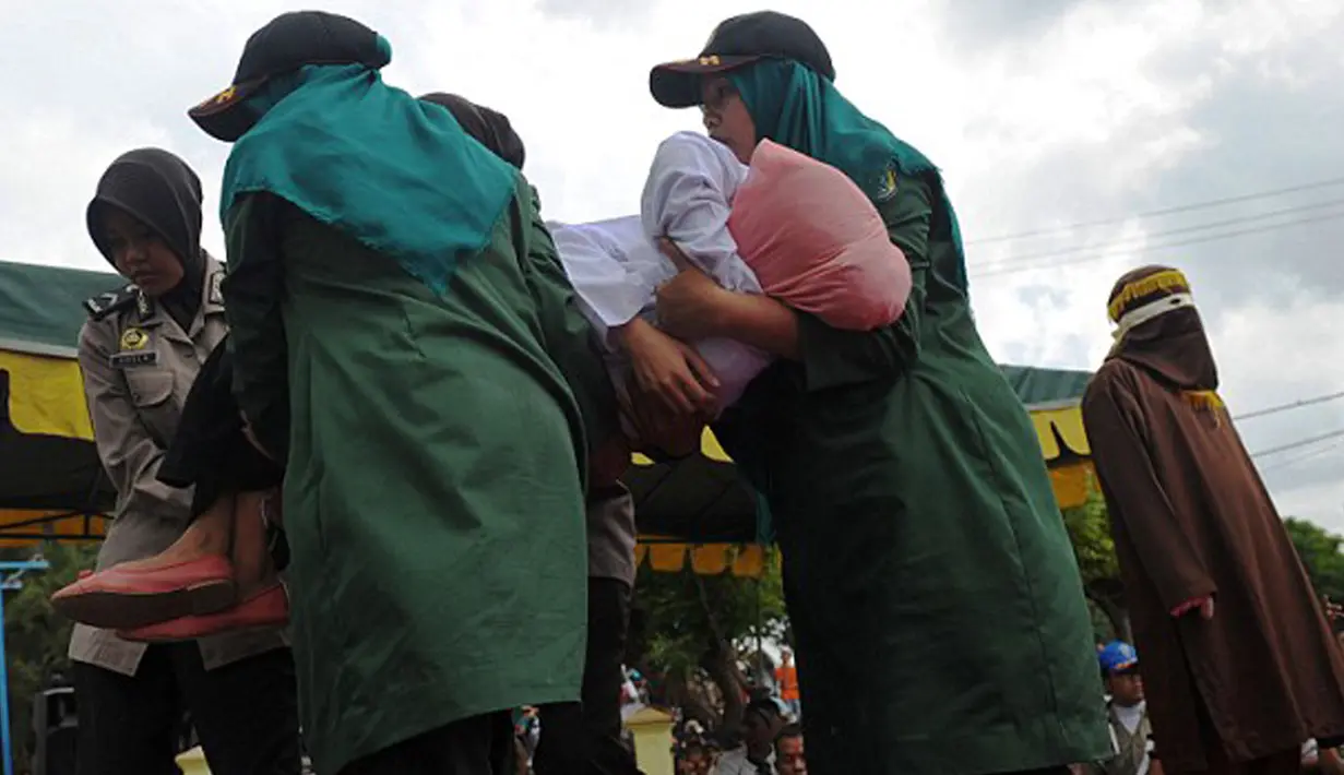 Petugas mengangkat Nur Elita, terpidana pelanggar hukum syariat, yang pingsan saat menjalani eksekusi hukuman cambuk di halaman Masjid Baiturrahim Ulee Lheue, Banda Aceh, Senin (28/12). (AFP/dailymail.co.uk)