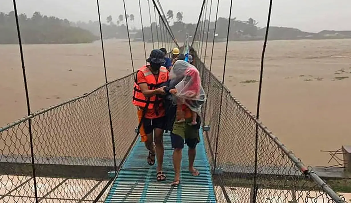 Tim penyelamat membantu warga menyeberangi jembatan saat dievakuasi di kota Tubay, Agusan del Norte, Filipina selatan, Kamis (16/12/2021). Puluhan ribu orang sedang dievakuasi ke tempat yang aman ketika Topan Rai mendekati pada Kamis (16/12). (Philippine Coast Guard via AP)