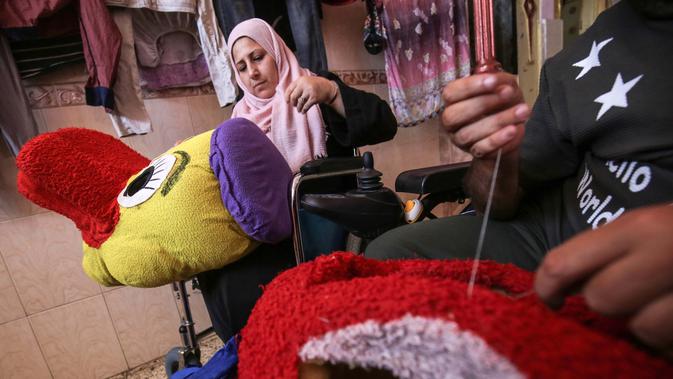 Nihad Jarboa (37) dan istrinya Zeinab (35), warga Palestina yang hidup dengan cacat fisik sejak masa kanak-kanak duduk di kursi roda mereka saat menjahit kostum yang terinspirasi kartun di rumah mereka di kamp pengungsi Rafah di selatan Jalur Gaza, pada 19 Juli 2020. (AFP Photo/Said Khatib)