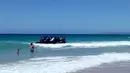 Seorang pria dan anak laki-laki menyaksikan  perahu karet yang dipenuhi imigran mendekati tepi pantai Cadiz di Spanyol selatan, 9 Agustus 2017. Puluhan imigran tersebut langsung melompat ke air dan berlarian menuju pantai. (Carlos Sanz via AP)