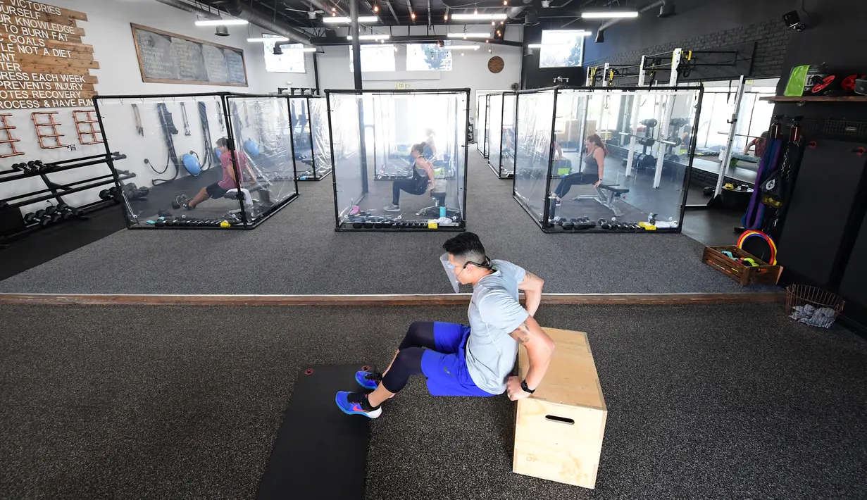 Peet Sapsin memimpin kelas dengan orang-orang berada dalam kotak plastik di Inspire South Bay Fitness di Redondo Beach, California pada 15 Juni 2020. Ruangan gym dengan plastik sebagai pemisah itu agar pengunjung dapat tetap berolahraga sambil tetap menjaga jarak fisik. (FREDERIC J. BROWN / AFP)