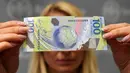 Seorang wanita menunjukkan uang kertas pecahan 100 rubel baru yang dirancang khusus untuk Piala Dunia 2018 di Moskow, Rusia, Selasa (22/5). Sekitar 20 juta uang kertas polimer akan dimasukkan ke dalam sirkulasi. (AFP/Kirill KUDRYAVTSEV)