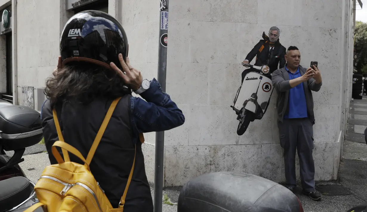 Seorang pria berselfie di dekat mural pelatih Jose Mourinho mengendarai skuter Vespa berhias lambang AS Roma di lingkungan Testaccio,  Roma (7/5/2021). Jose Mourinho dipecat Tottenham Hotspur pada 19 April kemarin. (AP Photo/Gregorio Borgia)